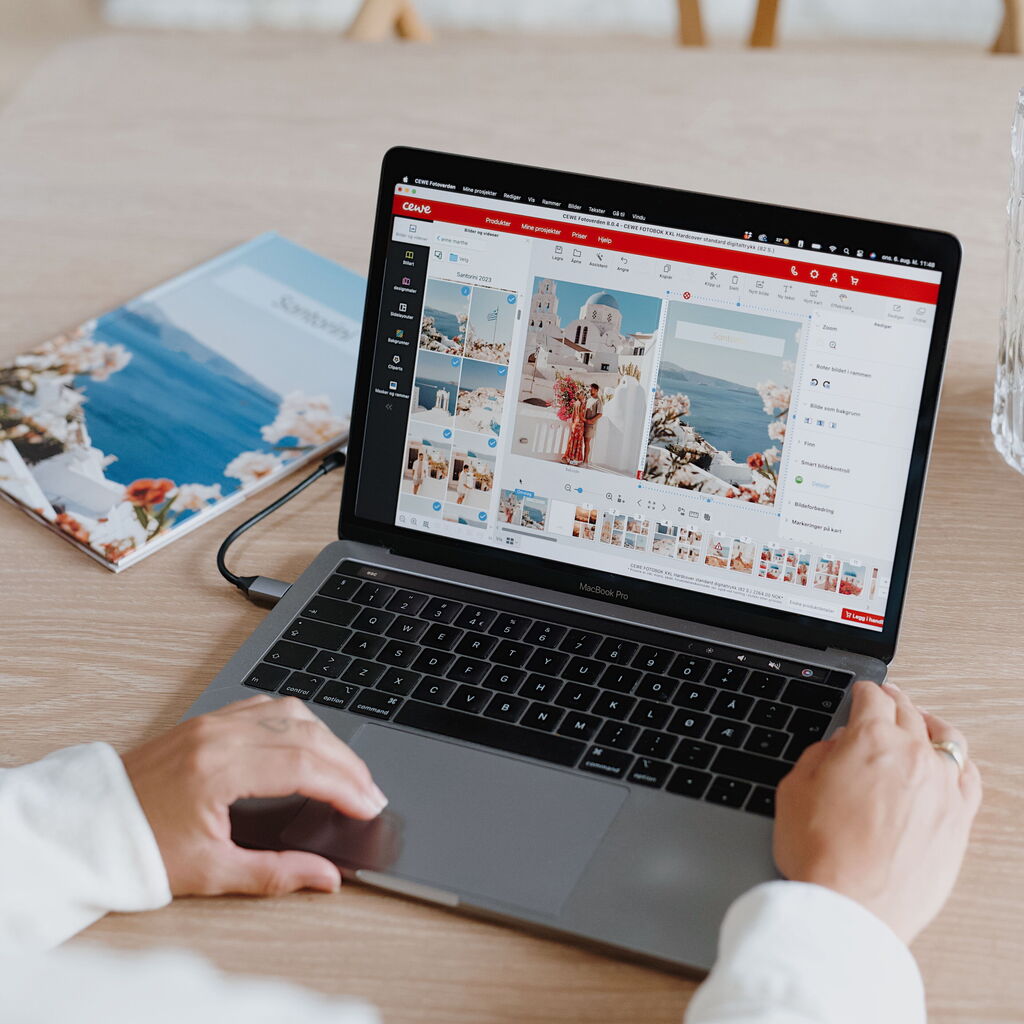 O persoană lucrează la laptop, așezată la masă. Pe ecran este deschis programul CEWE FOTOLUMEA, cu fotografii dintr-o vacanță.